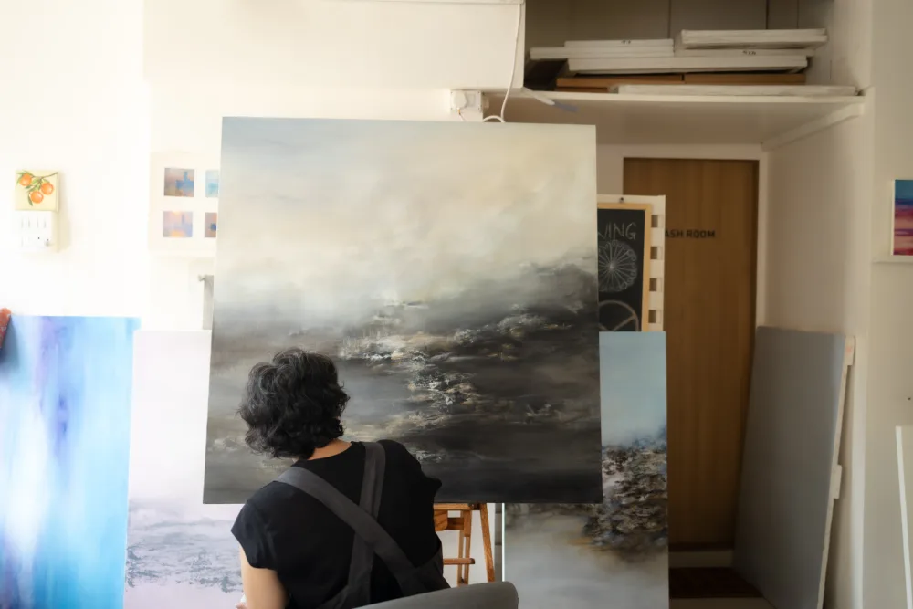 The artist contemplating a large landscape painting in her studio