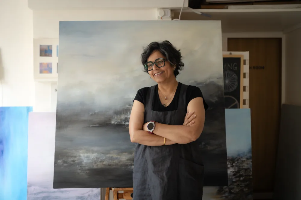 Reena Y. Ramakrishnan in her studio, before a large landscape painting